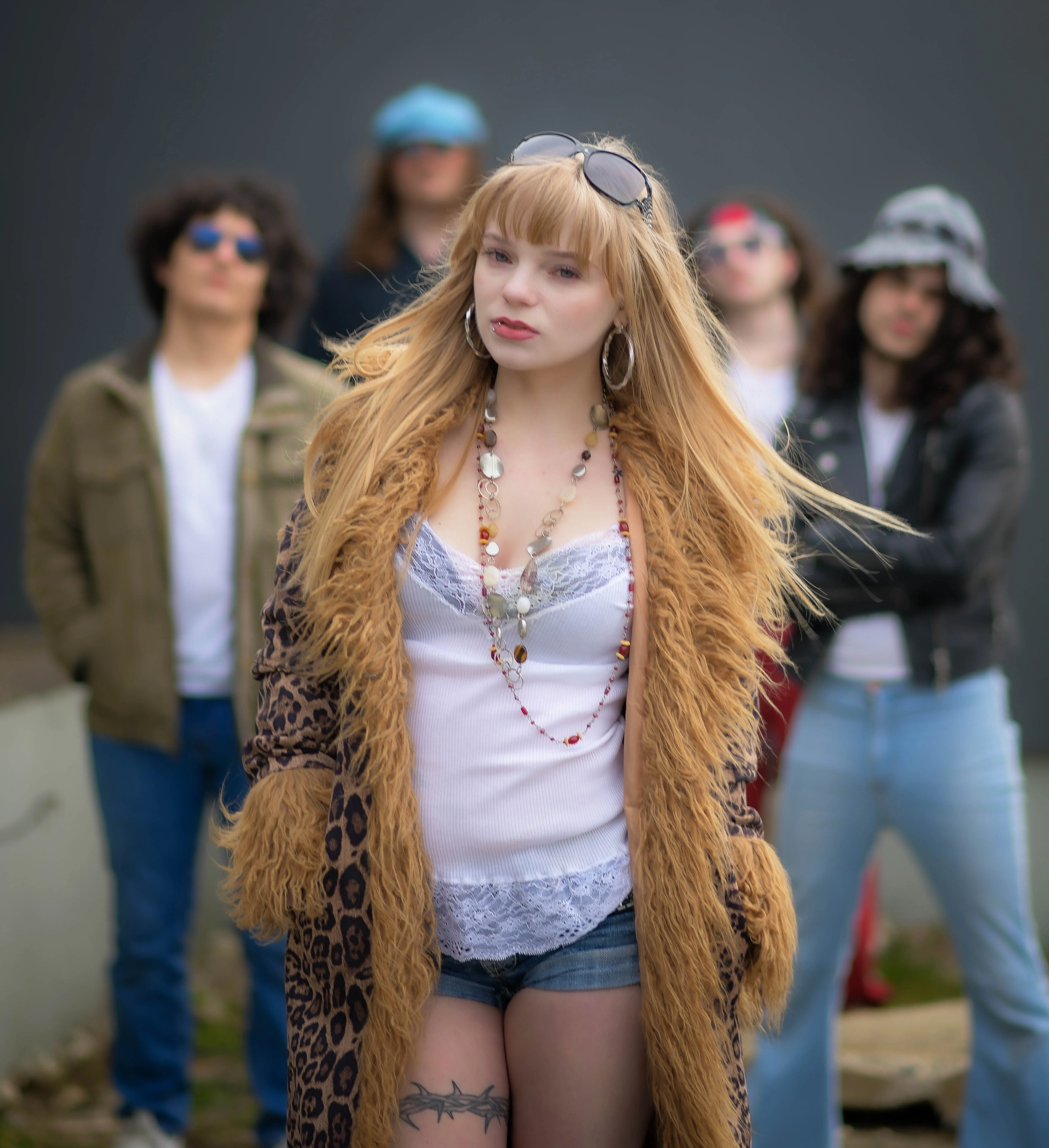 The five members of Suede Aces outdoors against a grey wall, the singer at the front in a shearling coat with the other four standing behind her